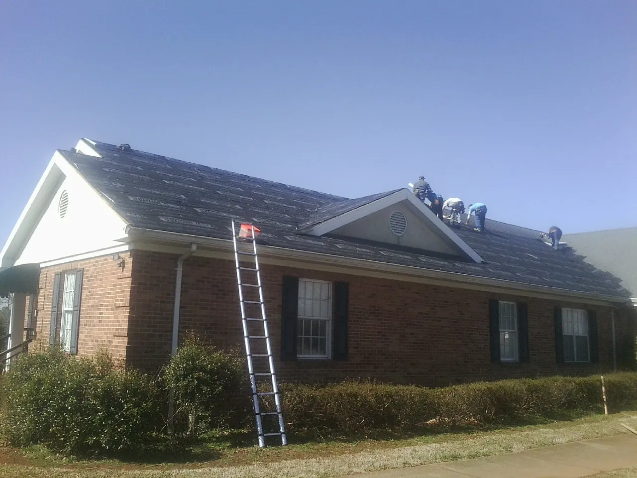 Crew tearing shingles off a brick ranch roof with a ladder set — Emergency Roof Repair work by our crew in Newton