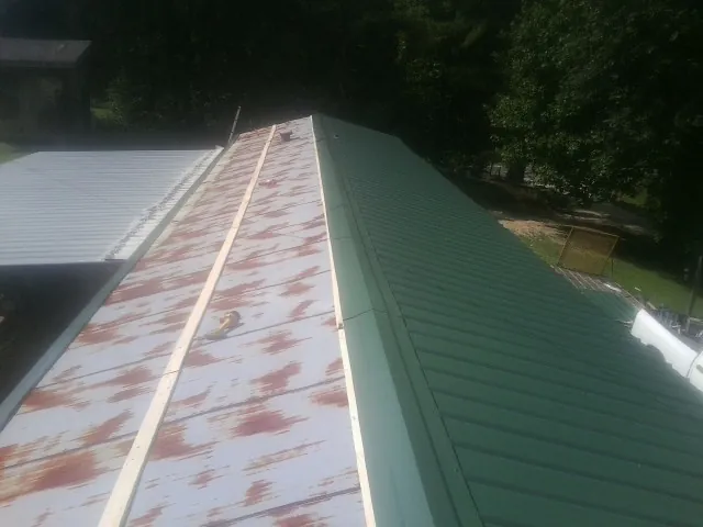 Old rusted panels beside newly installed green metal roofing — Wind Damage Roof Repair by Roofing Brothers in Newton