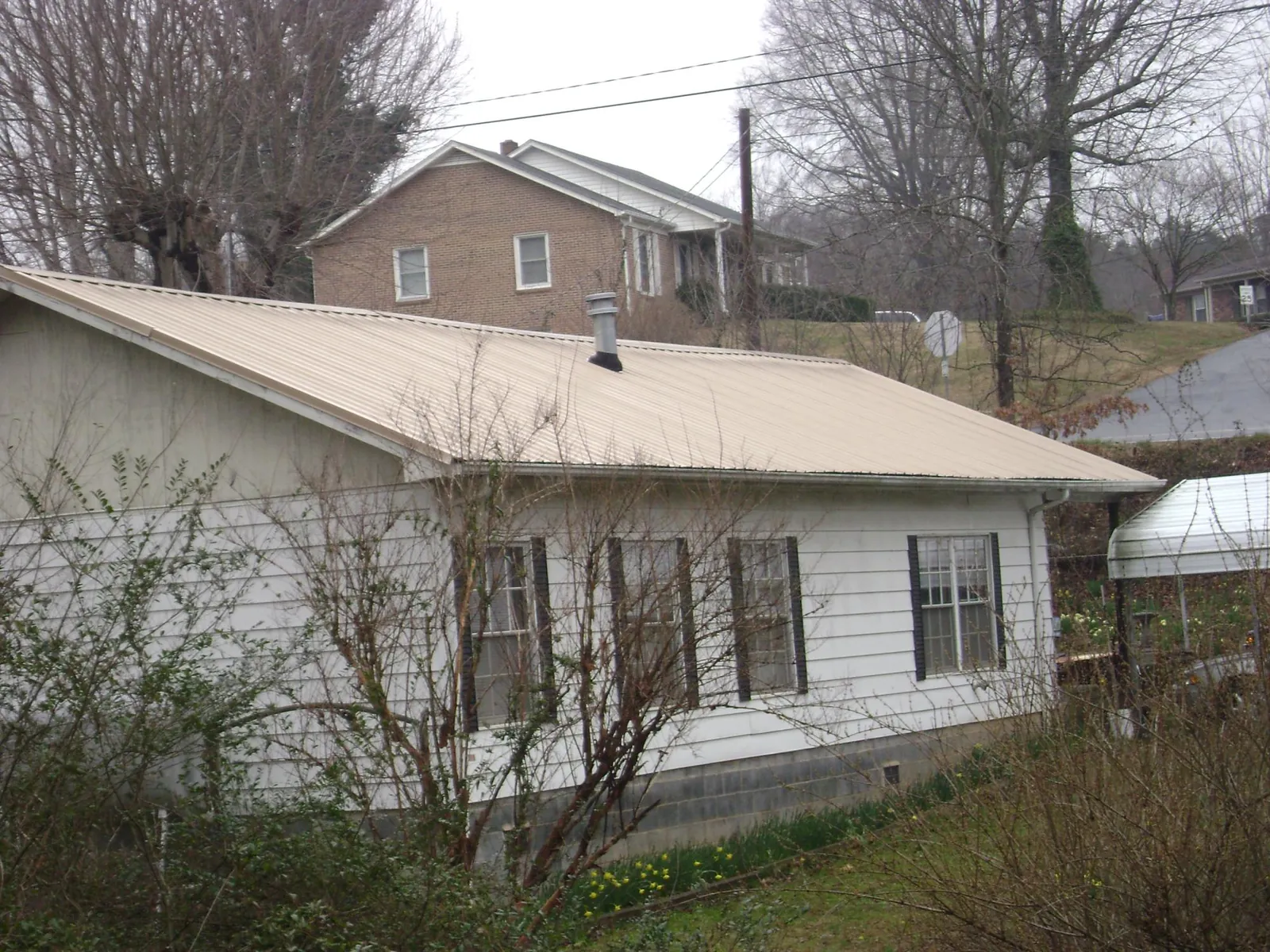 Tan metal roof on a white sided house set into a hillside — Commercial Roofing by Roofing Brothers in Newton